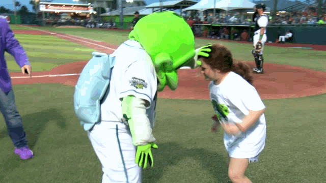 a little girl is standing next to a green mascot wearing a shirt that says ' champions ' on it