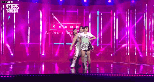 a group of women are dancing on a stage with purple lights behind them .