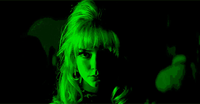 a woman with blonde hair is standing in a dark room with red and green lights behind her .