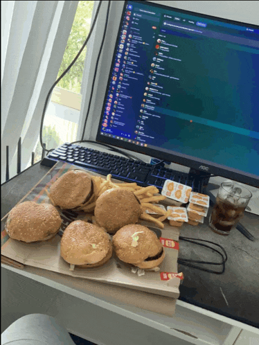 a bunch of hamburgers and french fries on a desk in front of an aoc computer monitor