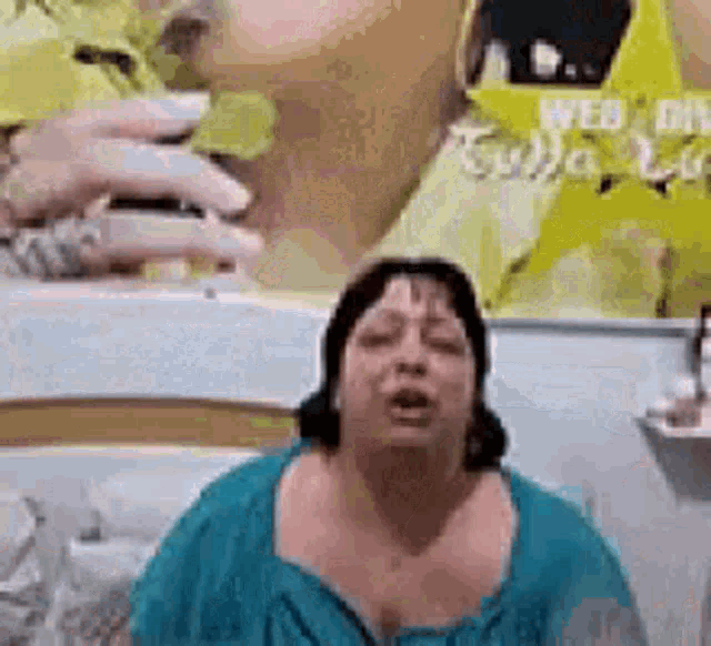 a woman in a blue shirt is making a funny face in front of a picture of a woman .