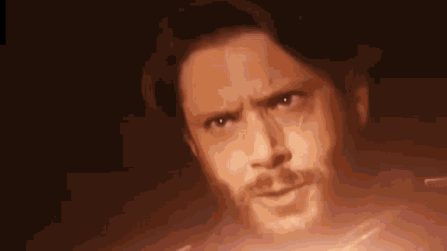 a close up of a man 's face with a beard and a red light behind him .