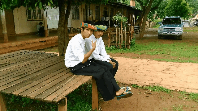 two boys sitting on a wooden bench with a car parked in the background that says ' toyota ' on it