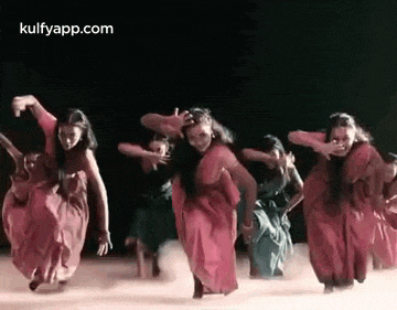 a group of women in red dresses are dancing on a stage in a dark room .