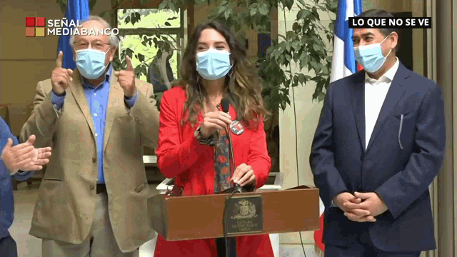 a woman wearing a red jacket stands at a podium with a sign that says lo que no se ve on it