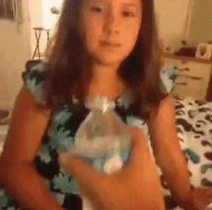 a girl in a blue and black floral dress is holding a plastic bag .