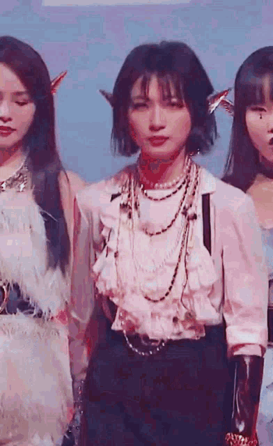 a group of women are standing next to each other on a stage . one of the women is wearing a ruffled shirt .