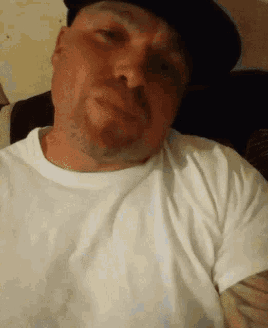a man wearing a hat and a white shirt is looking at the camera .