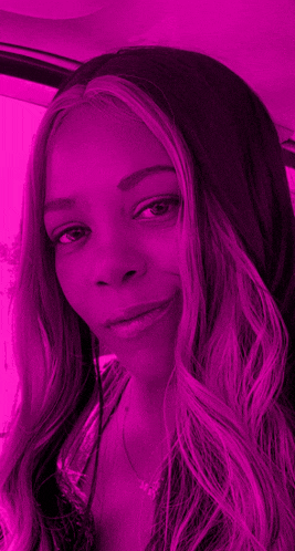 a woman with long purple hair is sitting in a car with a pink background .