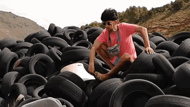 a man in a pink shirt is squatting down in a pile of tires