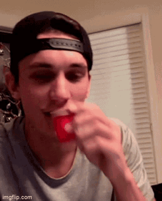 a young man wearing a baseball cap is eating a red cup ..