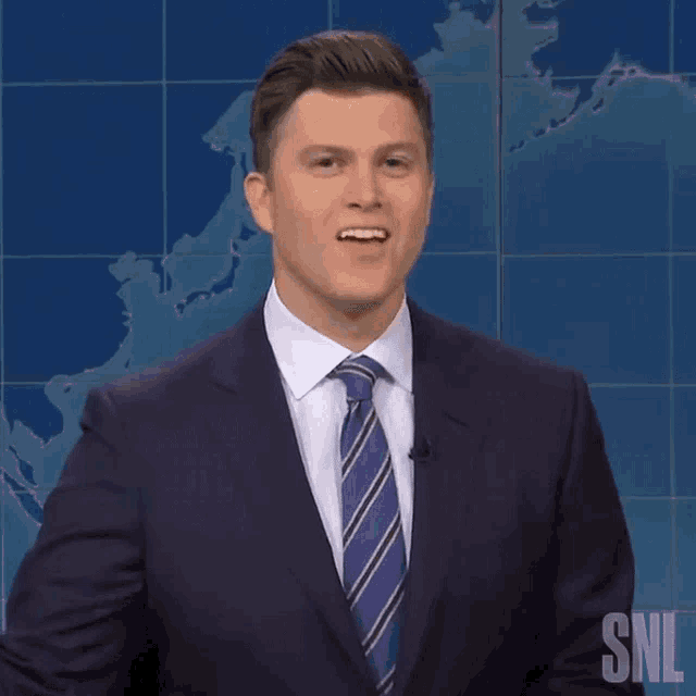a man in a suit and tie is standing in front of a snl logo