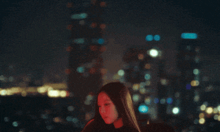a woman stands in front of a blurry city skyline at night