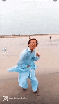 a man in a blue shirt and pants is dancing on the beach .