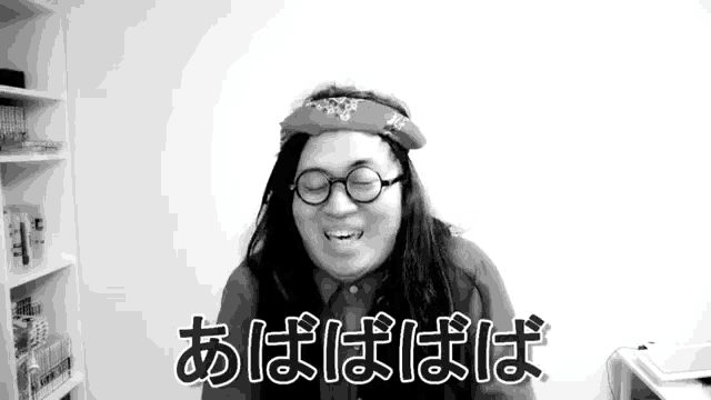 a man with long hair and glasses is wearing a bandana on his head and smiling in a black and white photo .