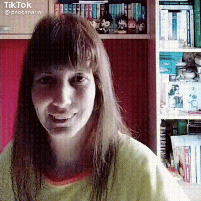 a woman with long hair is smiling in front of a bookshelf .