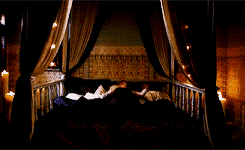 a woman is sitting on a bed with a canopy