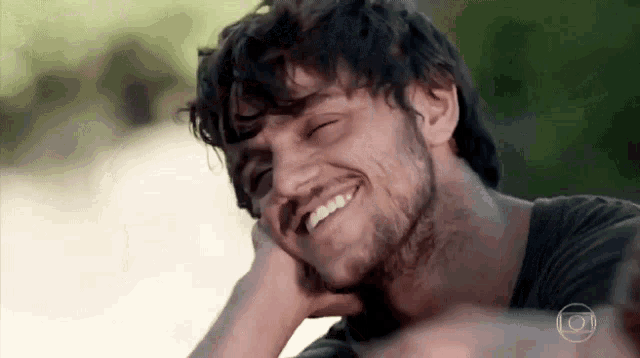 a man with a beard is smiling with his eyes closed and his hand on his face .