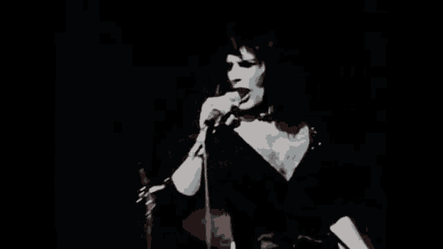 a man is singing into a microphone in a dark room with his hands outstretched .