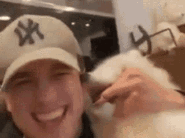 a man wearing a ny hat is taking a selfie with a cat .