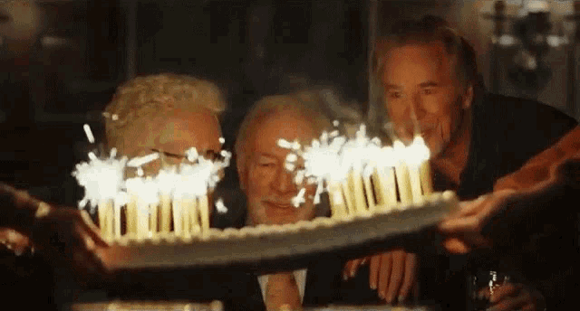 a group of men are blowing out candles on a cake