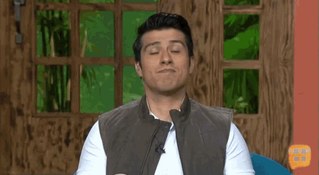 a man in a brown vest is covering his eyes with his finger