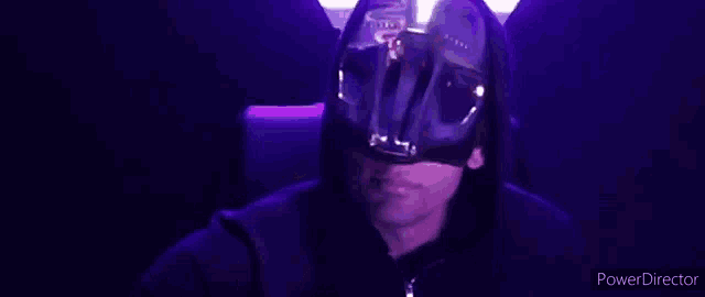 a man wearing a mask and a hooded jacket is sitting in a chair .