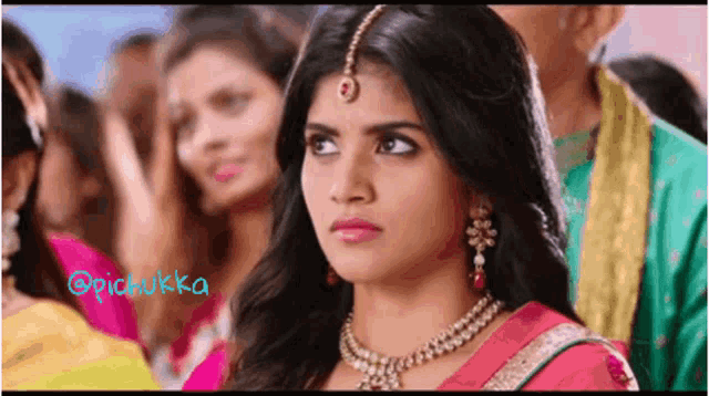 a woman in a pink sari and necklace is looking at the camera .