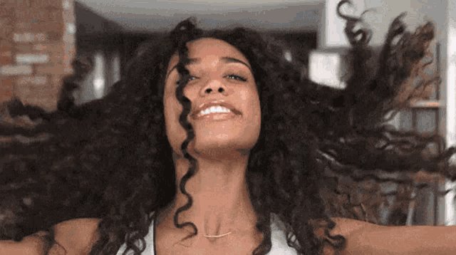 a woman with long curly hair is smiling with her arms outstretched and her hair is blowing in the wind .