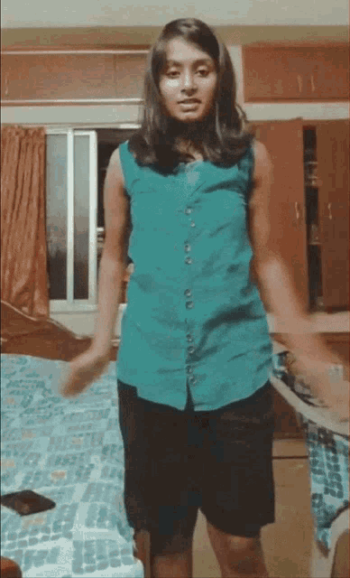 a girl in a blue shirt and black shorts stands in front of a bed