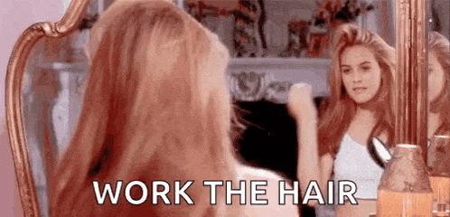 a woman is brushing her hair in front of a mirror with the words `` work the hair '' written on it .