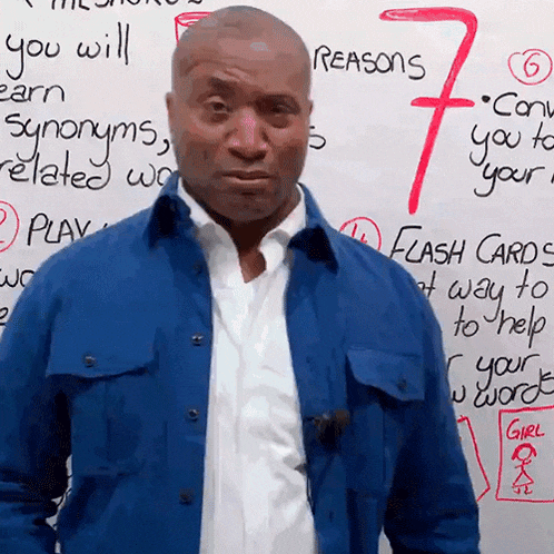 a man in a blue jacket stands in front of a white board that says reasons