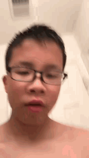 a boy wearing glasses is taking a bath in a bathroom .