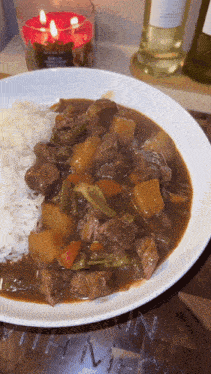 a plate of stew with rice and a candle behind it