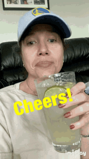 a woman wearing a golden state warriors hat is holding a glass of liquid with the words cheers written on it