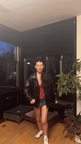 a woman wearing a leather jacket and shorts is dancing in a living room