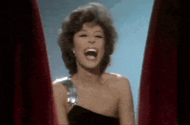 a woman in a black dress is laughing with her mouth open .