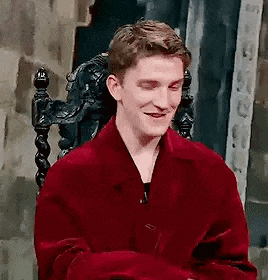 a man in a red jacket is sitting in a chair with his eyes closed and smiling .