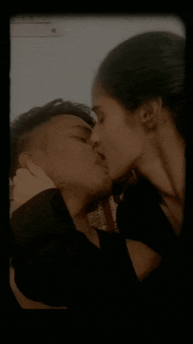 a man and a woman are kissing in front of a white wall