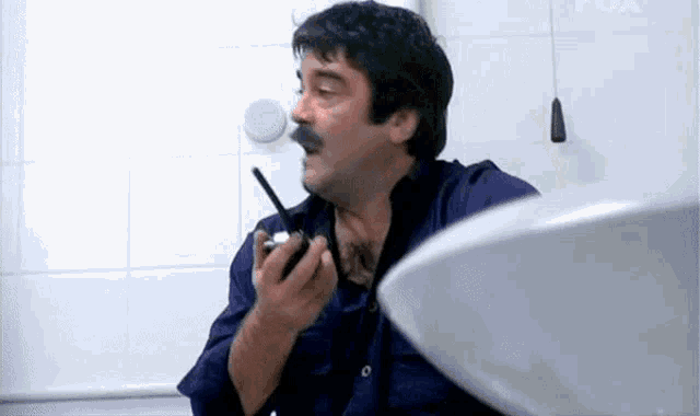 a man with a mustache is holding a walkie talkie in his hand in a bathroom .