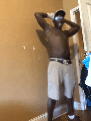 a shirtless man wearing shorts and a hat stands in a room