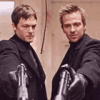 two men in suits and gloves are holding guns in their hands .