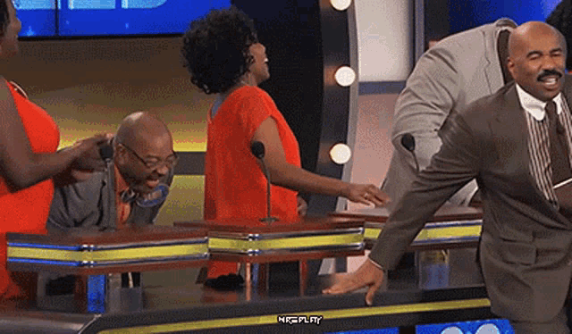 a man in a suit is standing next to a woman in an orange dress on a game show with replay written on the bottom