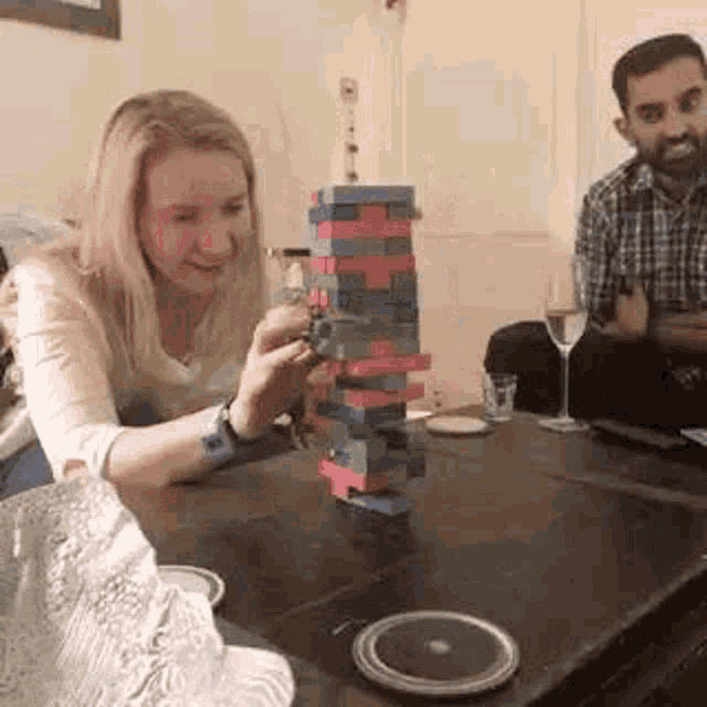 a woman is playing a game of jenga on a table with a man .