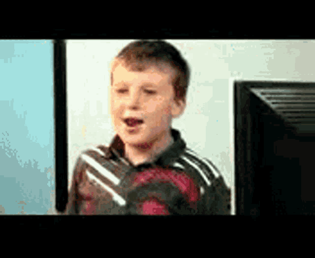 a young boy is standing in front of a computer monitor with his mouth open