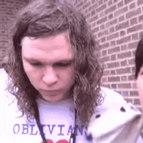 a young man with long curly hair is wearing a white shirt that says oblivia .