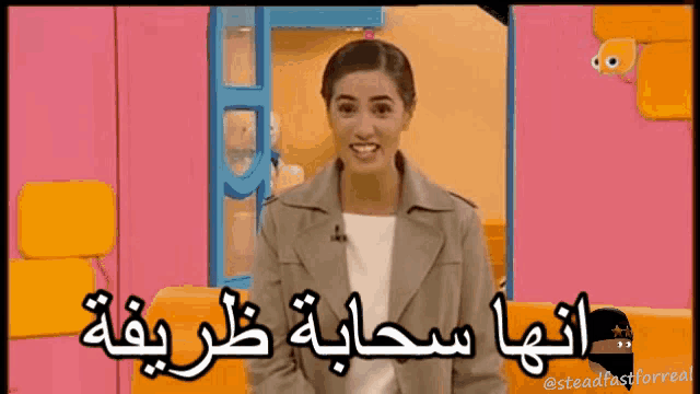 a woman is smiling in front of a pink wall with arabic writing