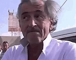 a man in a white shirt is standing in front of a car .