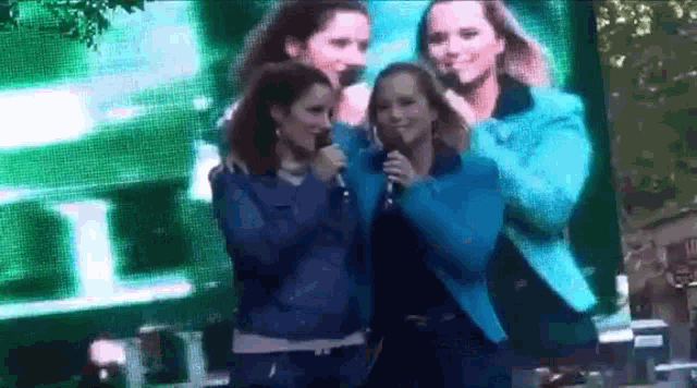 a group of women are singing into microphones in front of a large screen .