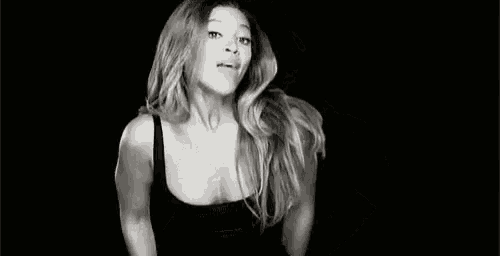 a black and white photo of a woman in a black tank top flexing her arms .
